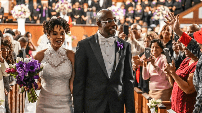 ouleye ndoye and raphael warnock together after their wedding ceremony, surrounded by joyful guests in a church setting.